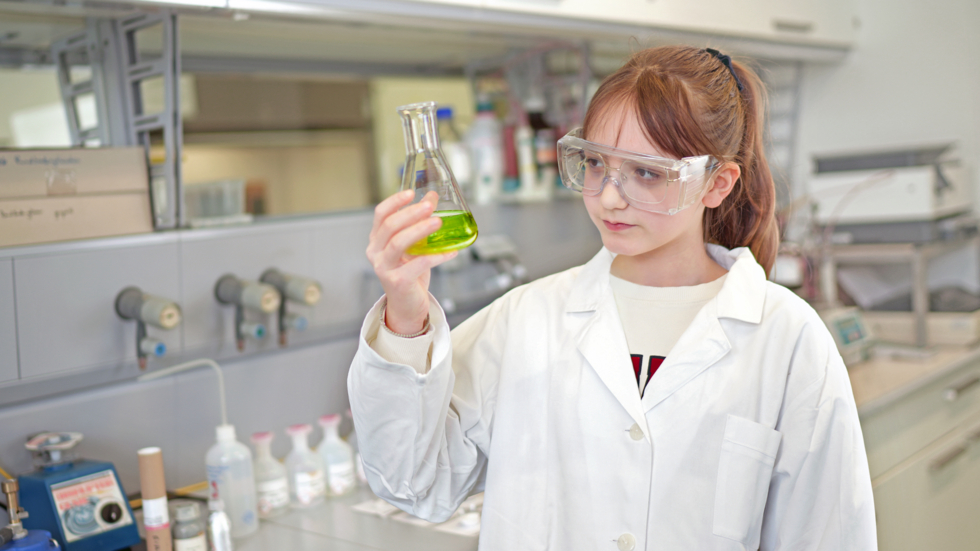 Mädchen in weißem Kittel mit Reagenzglas