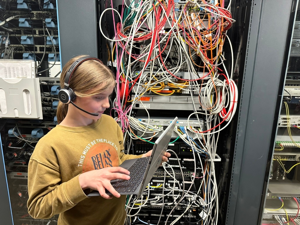 Mädchen mit Laptop steht vor einem Serverschrank.